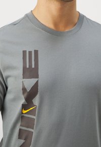 Grå bomulls-t-shirt med en tydlig Nike-logotyp i mörkgrått och gult, med rund halsringning och korta ärmar.