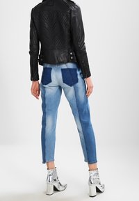 Svart läderbikerjacka med kviltad rygg, kontrasterande ljus- och mörkblå denimjeans med patchfickor, och silverfärgade klackstövlar i ankellängd.