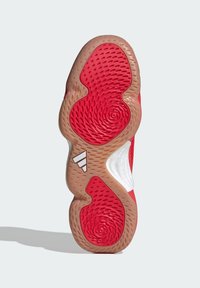 Shoe outsole in red and tan rubber with circular patterns. Features a white accent and branded three stripes logo. Textured for traction.