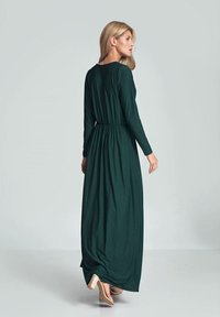 Maxi sukienka w głębokim zielonym kolorze, długie rękawy, okrągły dekolt, marszczona talia, zwiewna sylwetka, w połączeniu z beżowymi szpilkami.