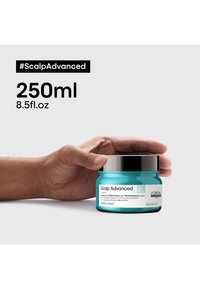 Turkosfärgad burk med Scalp Advanced-produkt, 250 ml, med svart skruvlock. Texten framhäver varumärket och användningen, hålls i en hand.