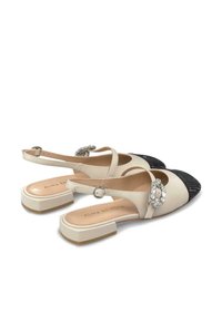 Scarpe slingback bicolore con corpo in pelle beige e punta nera testurizzata. Presentano un'applicazione in argento sul cinturino e un tacco a blocco.