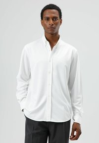 Weißes Hemd mit Knopfleiste, Kragen, langen Ärmeln und glatter Textur, getragen zu schwarzen Nadelstreifenhosen.