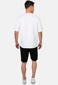 T-shirt blanc à manches courtes avec un col rond, associé à un short noir et des baskets blanches. Design simple, coupe décontractée, texture lisse.