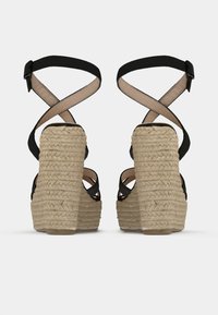 Black strappy platform sandals with woven espadrille heels, showcasing a textured beige rope design and adjustable ankle straps.