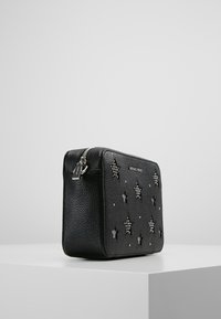 Czarna skórzana torebka na ramię z wytłaczanymi wzorami gwiazdek, srebrnymi ćwiekami i zapięciem na zamek. Kompaktowy prostokątny kształt z teksturowanym wykończeniem.