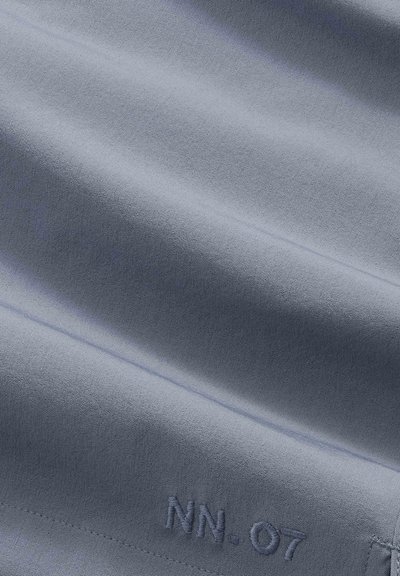 Smooth gray fabric with subtle folds and embroidered text "NN.07" near the bottom edge.
