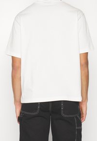 T-shirt blanc à manches courtes avec une coupe décontractée, doté d'un col rond et d'une texture en coton lisse. Le dos est uni sans embellissements.