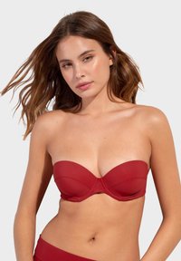 Červený bikiny top bez ramínek s hladkým povrchem, tvarovanými košíčky a švem uprostřed pro strukturu a oporu.