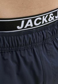 Tengerészeti úszónadrág elasztikus derékkal, fekete-fehér "JACK&J" logóval, sima textúrával és látható varrási részletekkel.