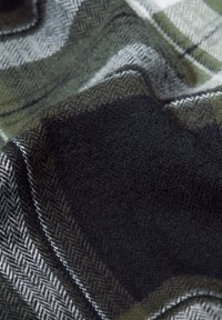 Coperta in lana con motivo a spina di pesce nei colori verde scuro, nero e grigio, caratterizzata da una texture morbida e sezioni a quadri variabili.