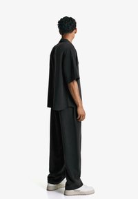 Camicetta nera a maniche corte e pantaloni larghi, realizzati in tessuto morbido. La camicia presenta una vestibilità rilassata; abbinata a sneakers bianche.