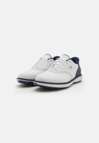 Chaussures de golf synthétiques blanches avec des accents navy, présentant des détails perforés, une pointe arrondie, une semelle plate et des lacets standards.