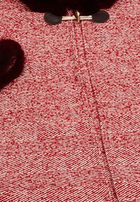 Röd och vit mönstrad textil med ett fiskbensmönster, med en mjuk textur och knäppningar för att stänga.