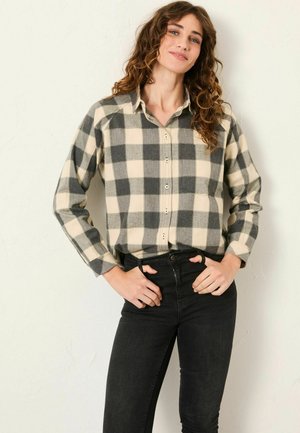 Gray and cream plaid flannel shirt with long sleeves, a button-down front, and a classic collar, paired with black jeans.