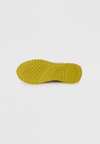 Sole of a shoe featuring a textured, rubberized surface in bright yellow with pattern grooves and a circular logo imprint.