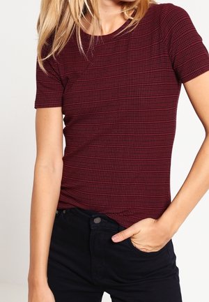 Bordeauxrotes eng anliegendes T-Shirt mit strukturiertem Karo-Muster, kurzen Ärmeln und rundem Ausschnitt, kombiniert mit dunklen Jeans.