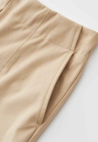 Pantaloni in suede beige con vita alta e tasche laterali visibili, mostrati su sfondo bianco.