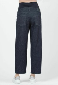 Jeans de pierna ancha de mezclilla oscura con una cinturilla elástica alta, que cuentan con dos bolsillos traseros y un acabado de tela texturizada. Llevados con zapatillas blancas.