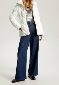 Chaqueta acolchada blanca con capucha, camiseta de manga larga a rayas negras y blancas, jeans de mezclilla oscuros de talle alto y pierna ancha, mocasines negros.