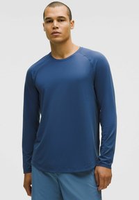 Langärmliges Sportshirt aus blauer feuchtigkeitsableitender Stoff mit Raglanärmeln und rundem Halsausschnitt, das eine glatte Textur aufweist.
