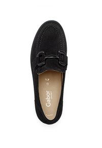 Zwarte suède instapschoen met een ronde neus, decoratieve zwarte hardware aan de voorkant, en een beige binnenvoering met het merknaam.