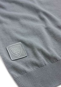 Maglione grigio lavorato a maglia con orlo a coste. Presenta una patch logo testurizzata in grigio più chiaro. Tessuto liscio con leggero effetto stretch.