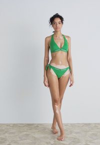 Grønt bikinitsett med halterneck-top og lavt liv med sidesnorer. Laget av glat materiale, med synlig merkevarelogo.