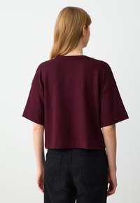 Bordeaux kortemouwen top met een relaxte pasvorm, voorzien van een ronde halslijn en zichtbare naden. Gekocht met een paar zwarte jeans. Eenvoudig, onversierd ontwerp.