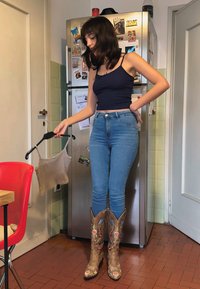 Beige gerippteres cropped Top an einem schwarzen Kleiderbügel; blaue hochtaillierte Jeans; braune Cowboystiefel mit floralen Stickereien; Küchenset.