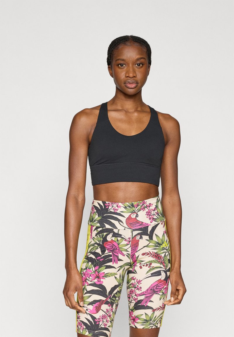 Sujetador deportivo negro y leggings estampados con pájaros rosas y hojas verdes sobre un fondo beige. Diseño ajustado, textura suave.