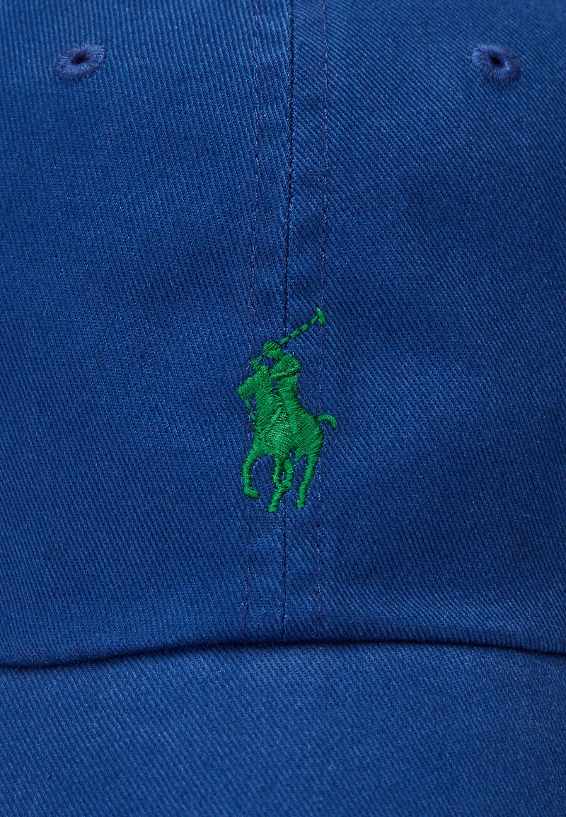 Casquette en coton bleu avec un logo brodé vert représentant un cheval et un cavalier à l'avant. Design structuré avec une visière courbée et un dos ajustable.