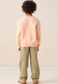 Sweatshirt pêche clair avec un col rond côtelé et des manches à poignet, associé à un pantalon large vert olive avec des poches arrière.