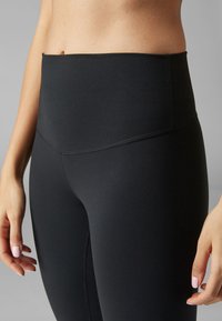 Leggings neri a vita alta realizzati in tessuto morbido e elasticizzato. Presentano una cintura ampia e dettagli cuciti lungo le gambe.