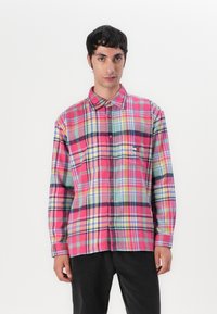 Pink plaid shirt with blue, yellow, and green accents. Features long sleeves, button front, and a chest pocket with logo detail.
