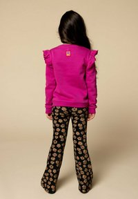 Fuchsia sweatshirt met gerimpelde mouwen en een logopatch, gecombineerd met zwarte flared broek met roze bloemenpatronen.