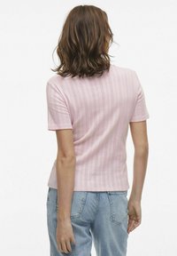Top corto rosa pallido a maniche corte con un motivo verticale testurizzato, design aderente e scollatura rotonda. Abbinato a jeans in denim blu.