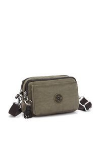 Olive green nylon crossbody bag with two zippered compartments, a logo patch, and a black fabric strap. Features silver hardware and a charm.
