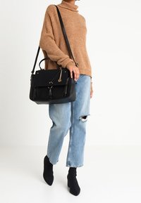 Schwarze Lederhandtasche mit goldenen Akzenten, strukturierte Form, ein Griff oben und ein langer Trageriemen. Getragen mit einem gemütlichen beigen Pullover und zerrissenen Jeans.