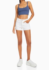 Blå croptop med tunna axelband, tillsammans med vita denimshorts med hög midja och uppvikta fållar. Bärs med vita sneakers.