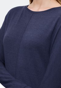 Maglione navy blu a maniche lunghe con scollatura rotonda e una finitura liscia e testurizzata. Presenta dettagli delle cuciture visibili sul davanti.