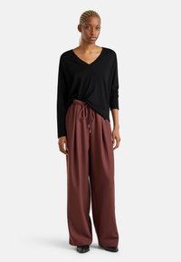 Maglione nero a V con maniche lunghe abbinato a pantaloni larghi bordeaux a vita alta, dotati di cordoncino e con texture liscia.