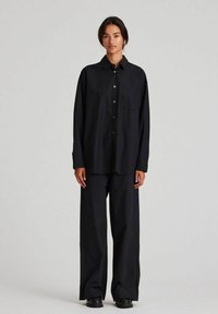 Camicia nera button-up con tasca, abbinata a pantaloni neri larghi. Entrambi i capi hanno una texture liscia e una vestibilità comoda.