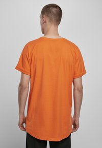 Tricou scurt cu mânecă scurtă, de culoare portocalie, cu o croială lejeră, cu mansete răsucite și un tiv rotunjit. Material din bumbac moale, design minimalist.