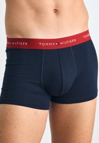 Sötétkék boxernadrág piros rugalmas derékkal, melyen fehér betűkkel olvasható a "TOMMY HILFIGER" felirat. Simaságot kínáló anyag és testhezálló fazon.