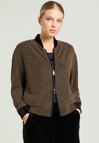 Bronzefarbene Metallic-Bomberjacke mit Frontreißverschluss, schwarzem Samtkragen und -bündchen, strukturiertem Stoff und lockerem Schnitt.