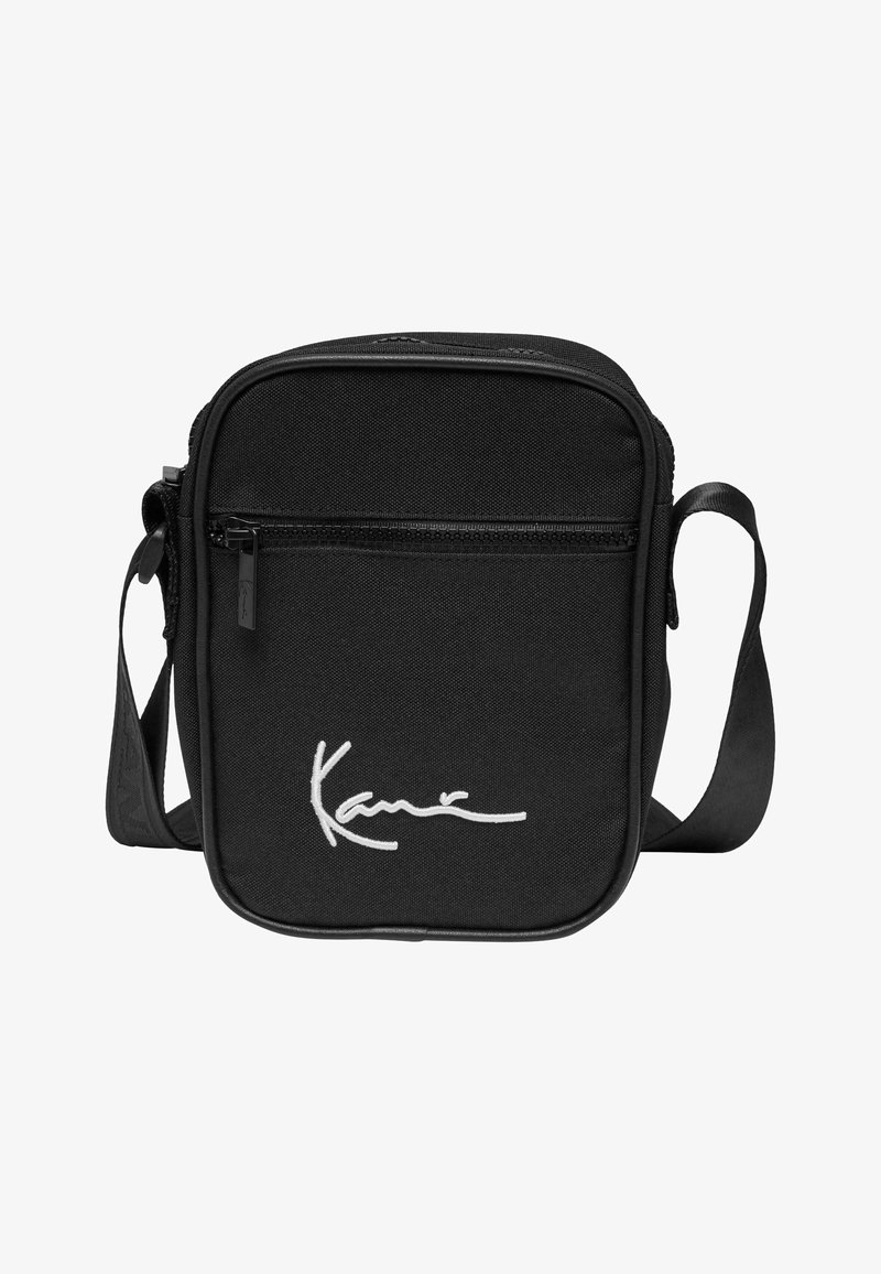 Crna crossbody torba izrađena od izdržljive tkanine, s prednjim džepom na patentni zatvarač i bijelim potpisom. Podesiva traka za praktičnost.