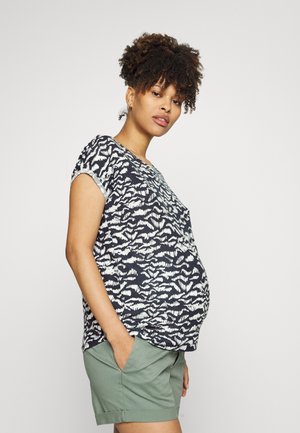 Blusa de maternidade em azul marinho com padrão abstrato branco, mangas curtas e corte descontraído. Acompanhada por calções verdes, com bolsos laterais.
