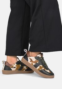 Sneaker mit einer Mischung aus Kuhmuster und schwarzem Leder, grünen Schnürsenkeln und einem braunen Absatz. Gummisohle, lässiges sportliches Design.