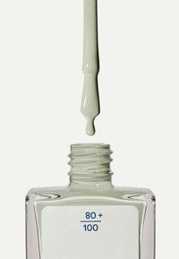 Ljust grönt nagellack i en klar glasflaska. Flaskan har en platt form och en rund nacke, med en vit etikett som visar "80 + 100."